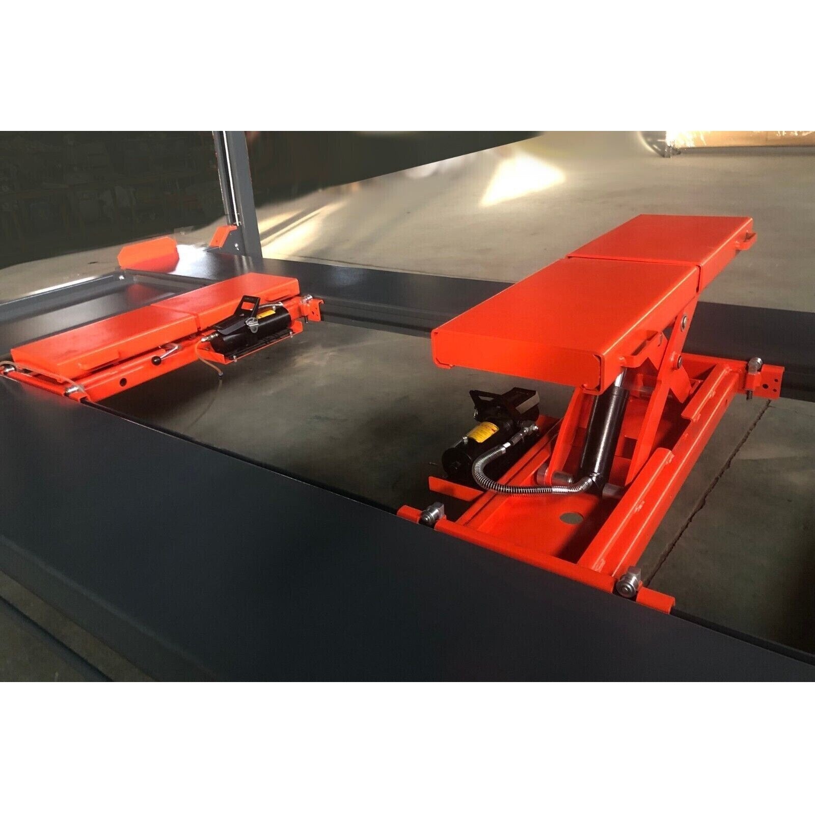 Red rolling jack platform with lift arms and black hydraulic pump handle