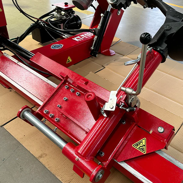 Red tire changer platform with clamps and hydraulic rod near a mounted wheel area