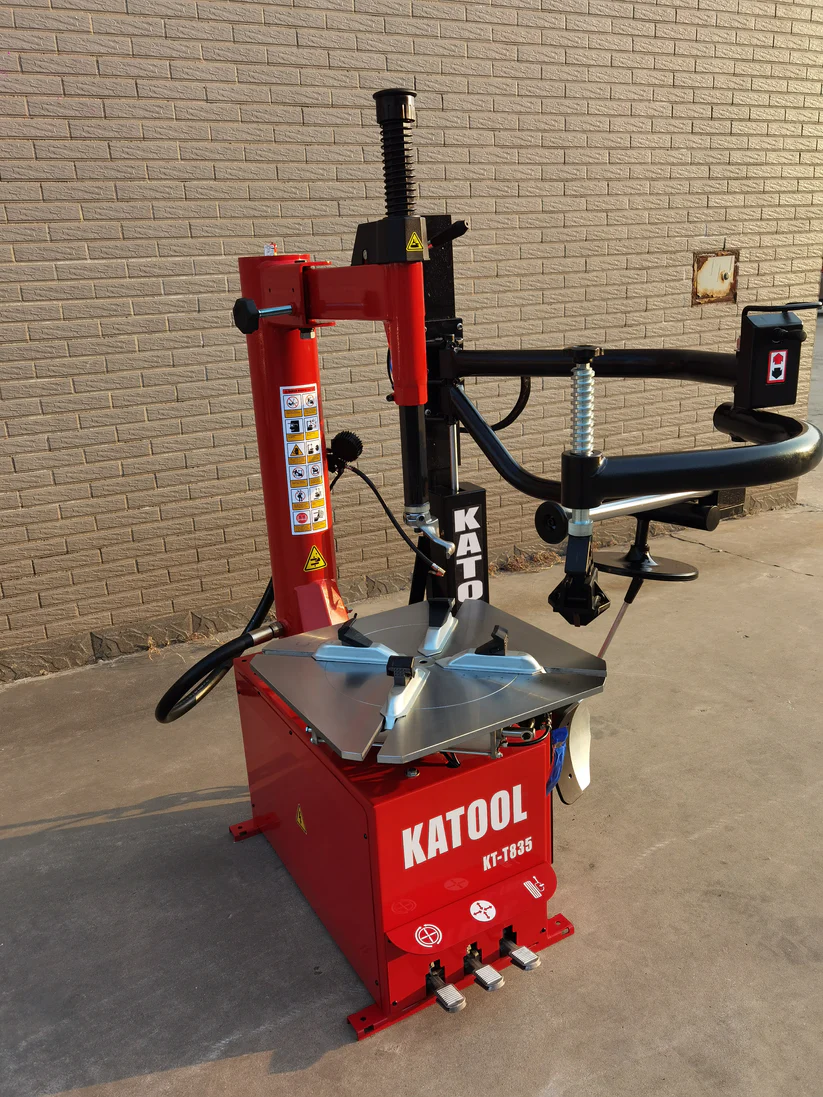 Double-arm tire changer with assist post and silver mounting table, red base and black arms