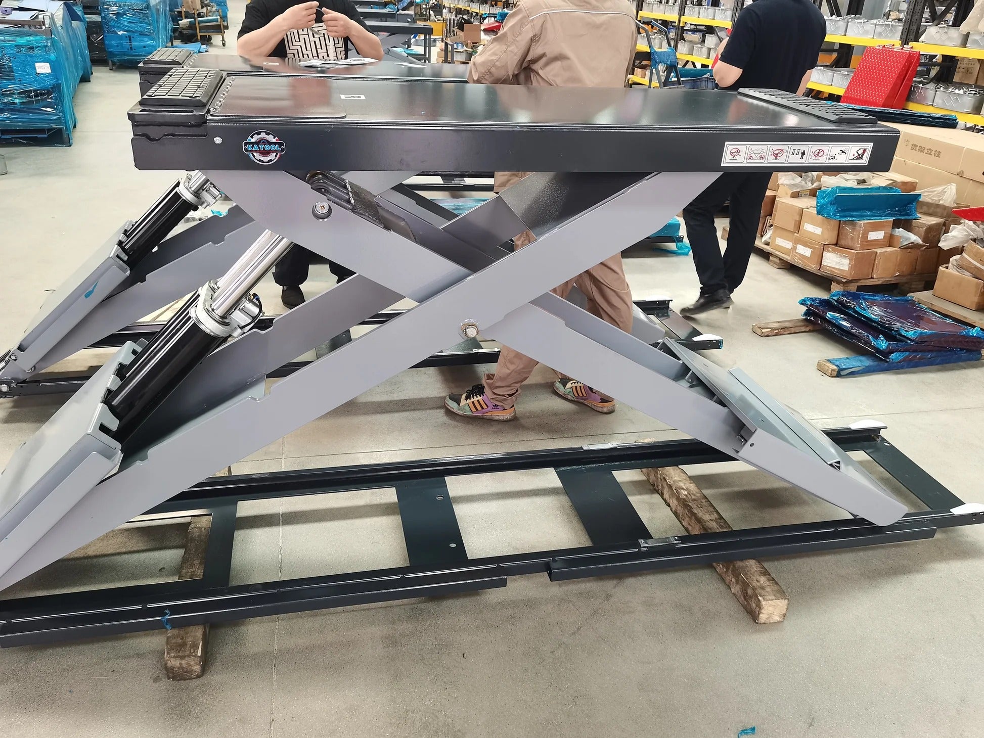 Full-rise scissor lift in assembly with gray frame, hydraulic cylinders, and black base rails