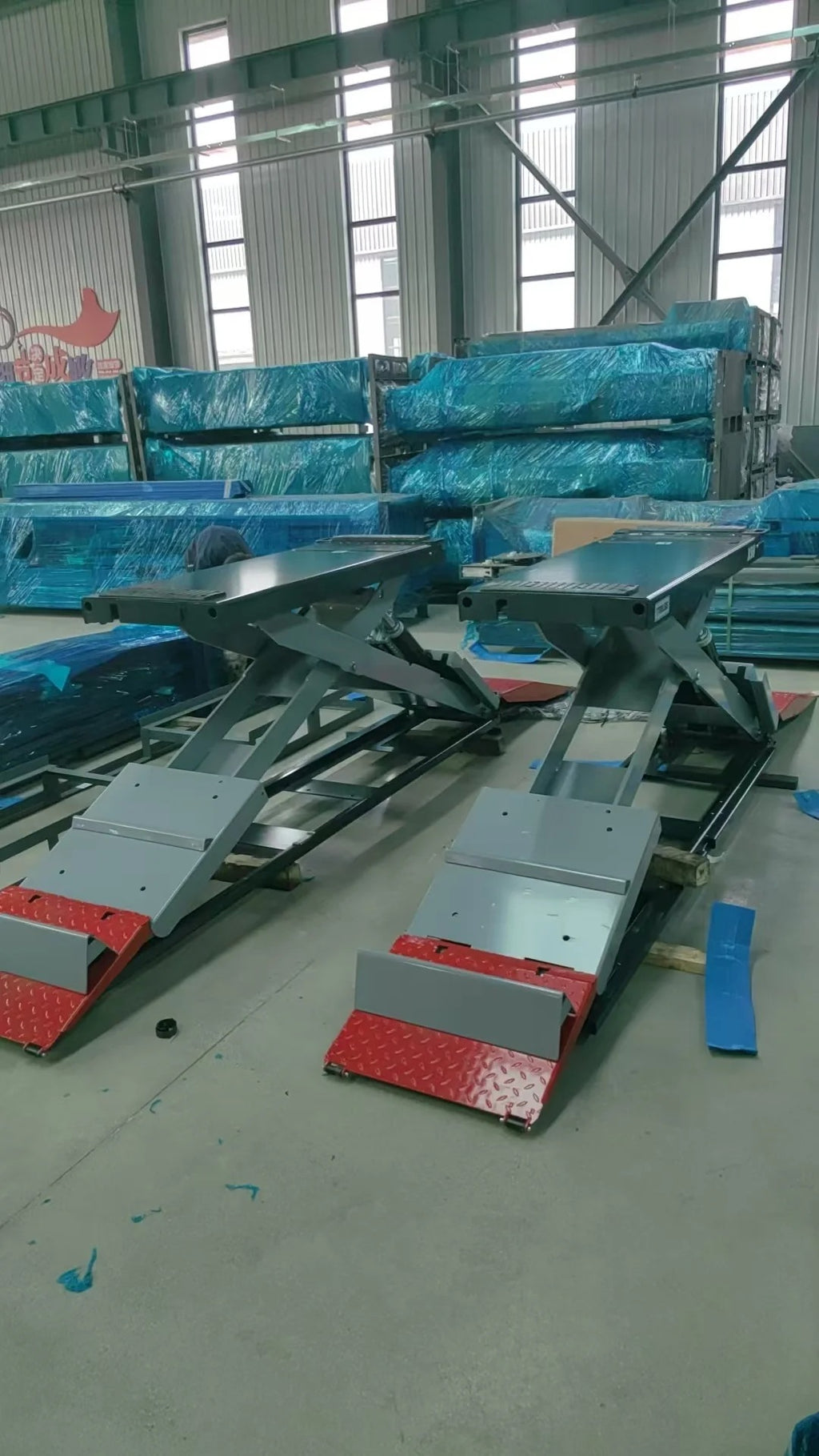 Full-rise scissor lift in workshop with multiple gray lift frames and red platform pads
