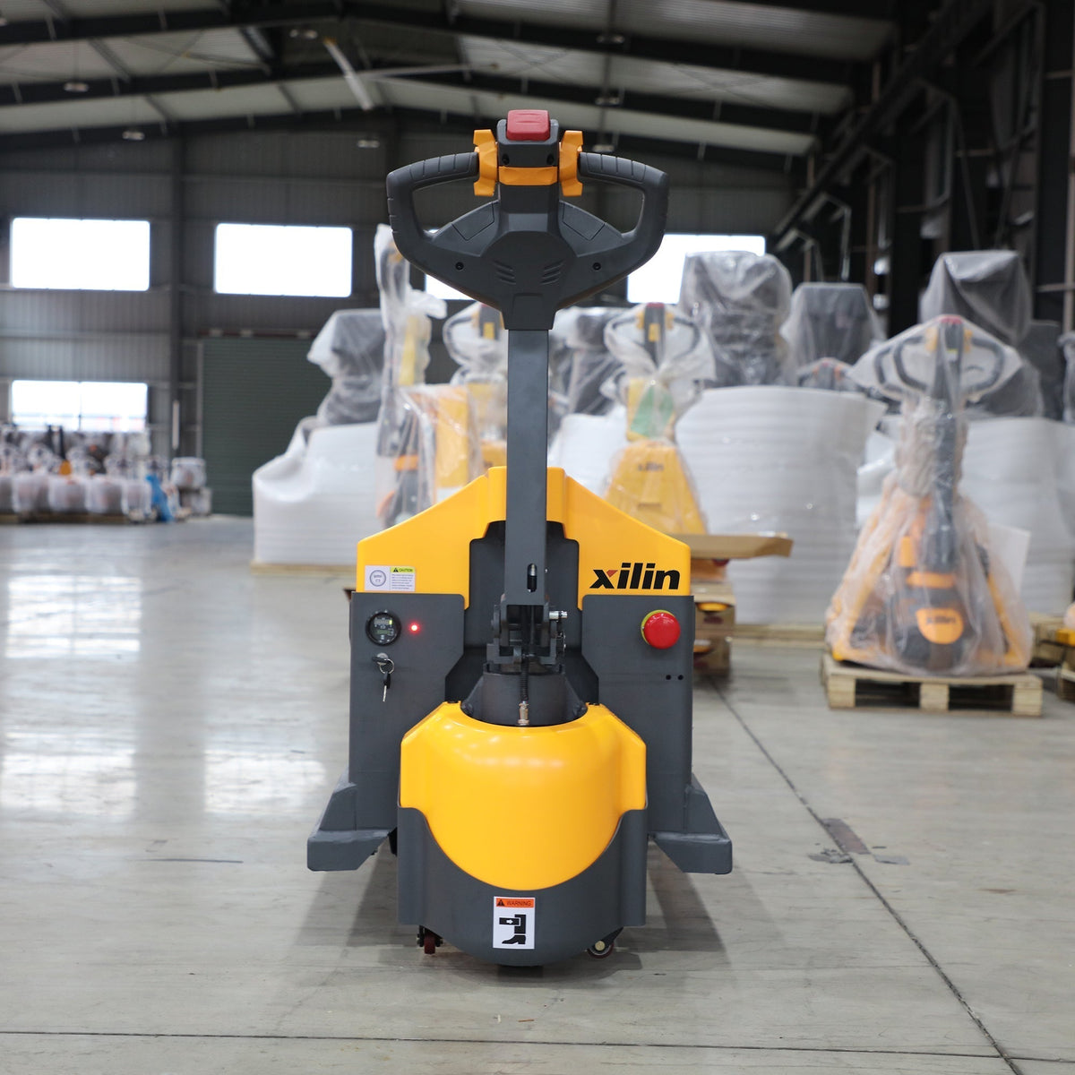 Electric pallet jack with orange/yellow body and black forks in warehouse setting