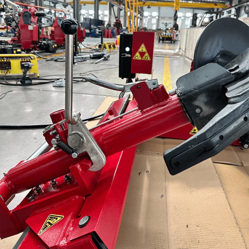 Red tire changer with black mounting arm and lever, positioned on shop floor
