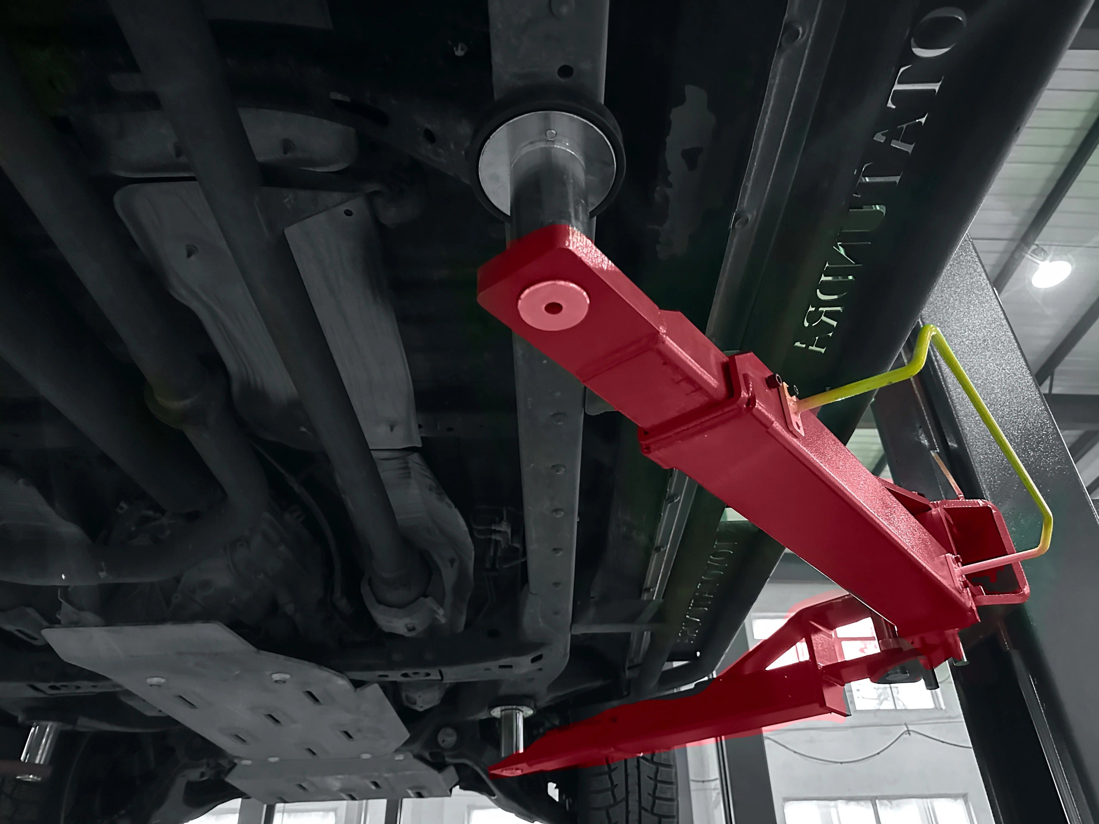 Red safety arm and linkage under a two-post vehicle lift